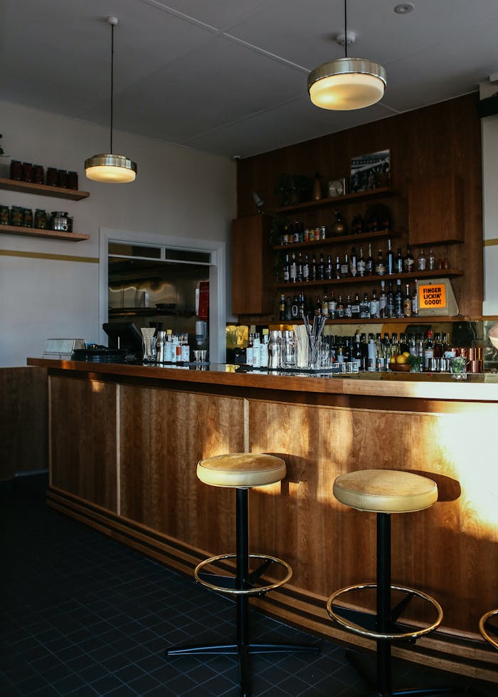 Warm and inviting pub interior featuring a wooden bar counter with stools and shelves of bottles.
